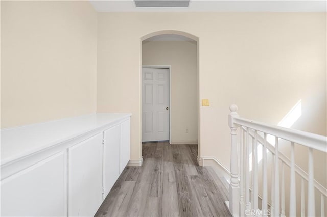 corridor with visible vents, arched walkways, baseboards, an upstairs landing, and light wood-style floors