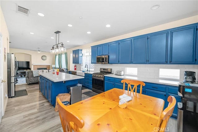 kitchen with visible vents, a kitchen island, appliances with stainless steel finishes, blue cabinetry, and a sink