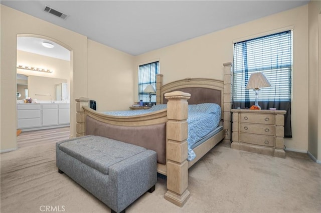 carpeted bedroom with ensuite bath, visible vents, and baseboards