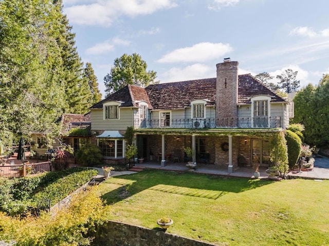 rear view of house featuring a lawn, a patio area, and a balcony