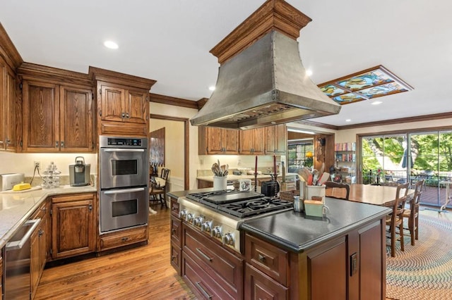 kitchen with appliances with stainless steel finishes, ornamental molding, island range hood, a center island, and light hardwood / wood-style floors