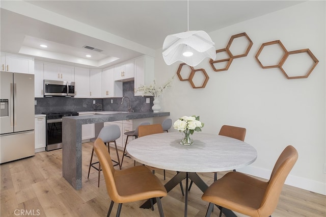 dining area with a raised ceiling, sink, and light hardwood / wood-style flooring