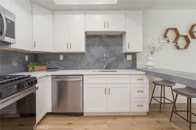 kitchen with white cabinets, stainless steel appliances, light wood-type flooring, and sink