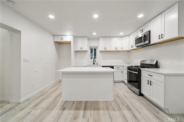 kitchen with light wood-type flooring, a center island, sink, white cabinetry, and appliances with stainless steel finishes