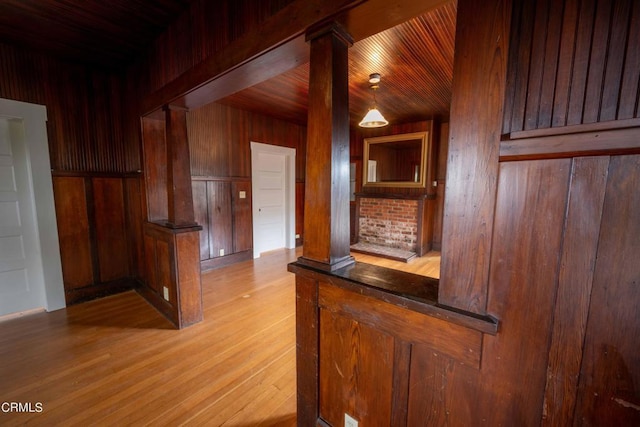 bar with hanging light fixtures, wooden walls, light hardwood / wood-style flooring, wood ceiling, and decorative columns