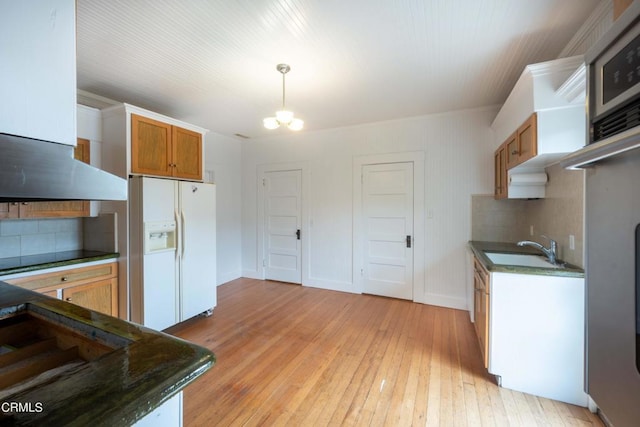 kitchen featuring white refrigerator with ice dispenser, backsplash, decorative light fixtures, and sink