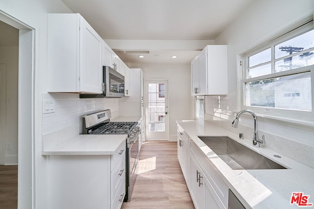 kitchen featuring appliances with stainless steel finishes, backsplash, sink, light hardwood / wood-style flooring, and white cabinetry