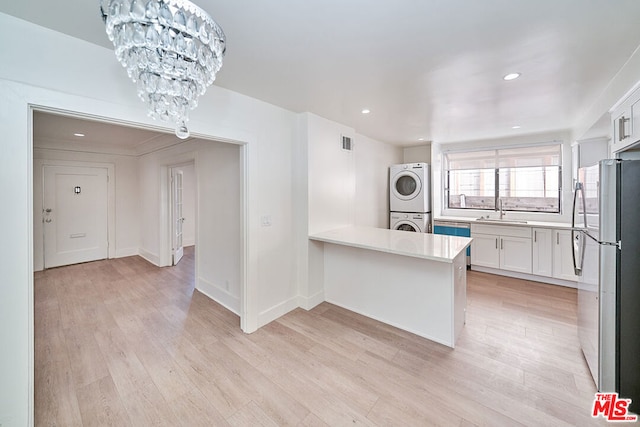 kitchen featuring sink, stacked washer and dryer, white cabinetry, stainless steel appliances, and a chandelier