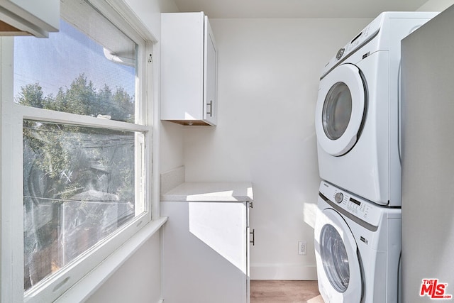 clothes washing area featuring cabinets, stacked washer / drying machine, and light wood-type flooring