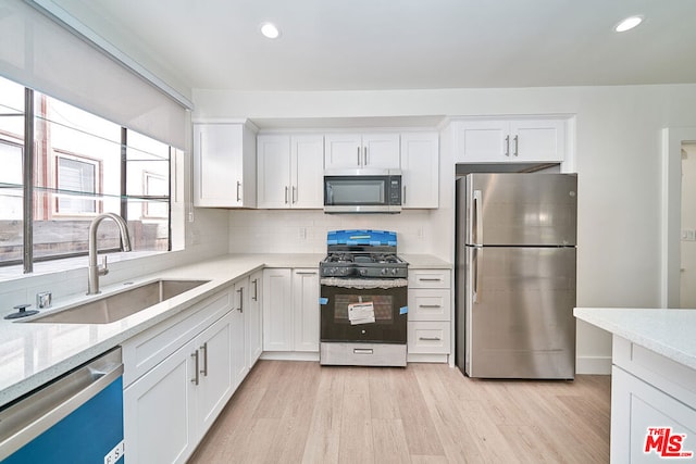 kitchen featuring sink, stainless steel appliances, light hardwood / wood-style flooring, decorative backsplash, and white cabinets