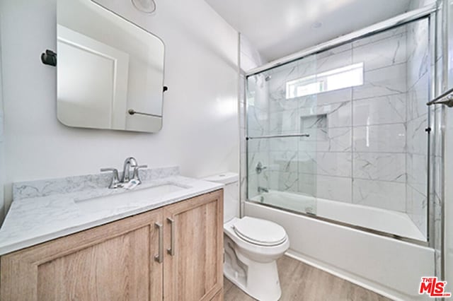 full bathroom with combined bath / shower with glass door, vanity, hardwood / wood-style flooring, and toilet