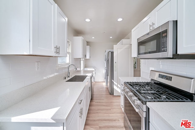 kitchen with white cabinetry, sink, stainless steel appliances, light stone counters, and light wood-type flooring