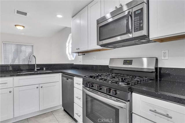 kitchen with stainless steel appliances, sink, dark stone countertops, white cabinets, and light tile patterned flooring