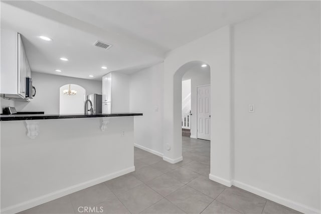 kitchen with kitchen peninsula, a kitchen breakfast bar, stainless steel appliances, light tile patterned floors, and white cabinetry