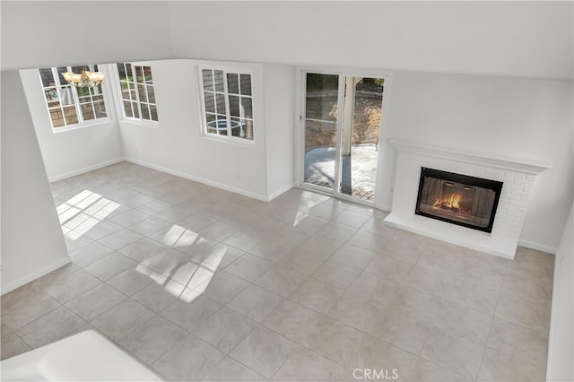 unfurnished living room with an inviting chandelier, light tile patterned floors, lofted ceiling, and a brick fireplace