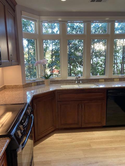 kitchen with light wood-type flooring, light stone countertops, sink, and black appliances