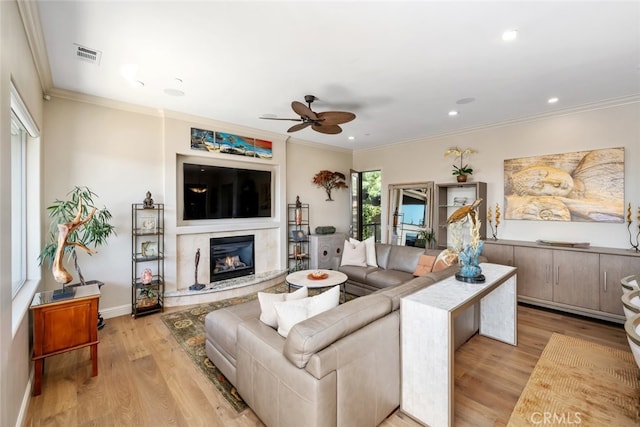 living room featuring light hardwood / wood-style floors, ornamental molding, ceiling fan, and a premium fireplace