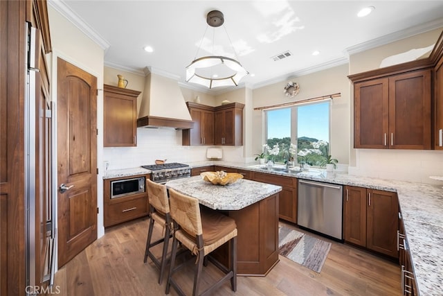 kitchen with custom exhaust hood, appliances with stainless steel finishes, hanging light fixtures, and light hardwood / wood-style floors