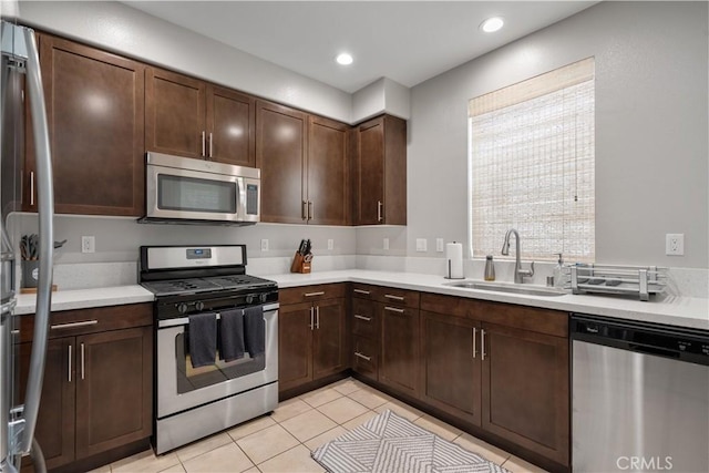 kitchen featuring stainless steel appliances, sink, light tile patterned floors, and dark brown cabinetry