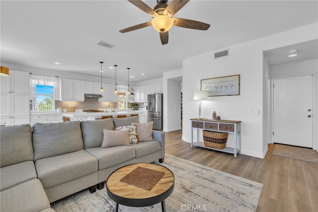 living room with light wood-type flooring, ceiling fan, and sink