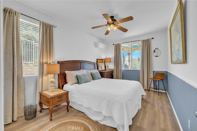 bedroom with multiple windows, light hardwood / wood-style floors, ceiling fan, and a wall unit AC