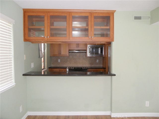 kitchen with decorative backsplash, stainless steel microwave, light hardwood / wood-style flooring, and a wealth of natural light