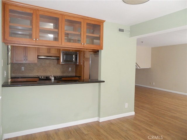 kitchen with light wood-type flooring, backsplash, kitchen peninsula, and appliances with stainless steel finishes