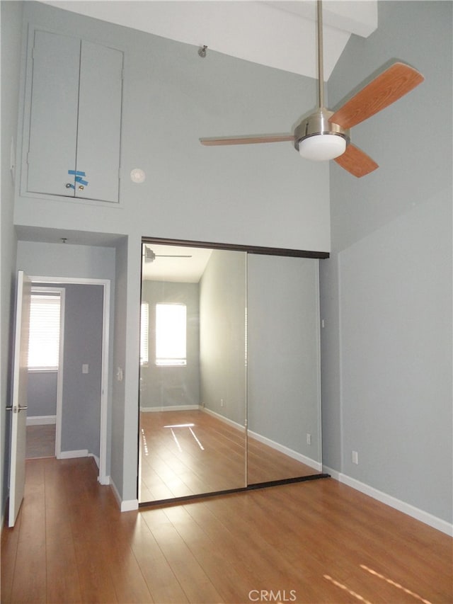 unfurnished bedroom with high vaulted ceiling, a closet, beamed ceiling, and hardwood / wood-style flooring