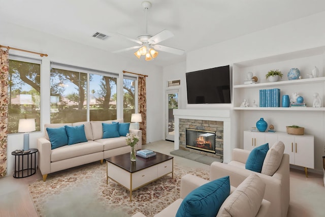 living room featuring ceiling fan, a stone fireplace, and light wood-type flooring