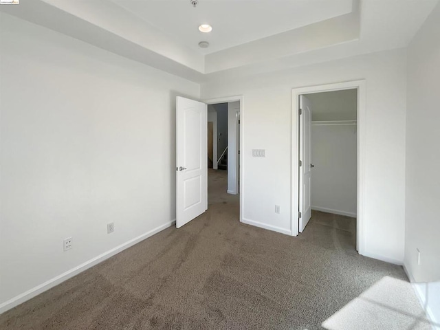 unfurnished bedroom featuring a walk in closet, carpet floors, a tray ceiling, and a closet