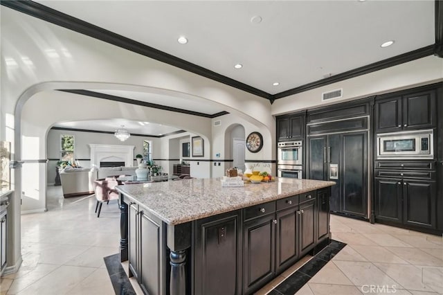 kitchen with a kitchen island, crown molding, built in appliances, light stone countertops, and light tile patterned floors