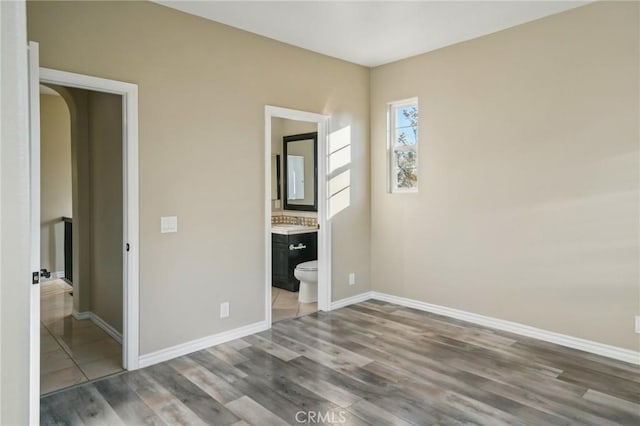 unfurnished bedroom featuring wood-type flooring and ensuite bath