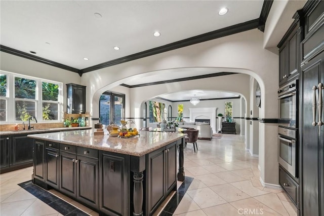 kitchen with light tile patterned floors, a center island, ornamental molding, light stone counters, and sink