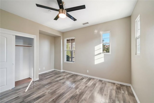 unfurnished bedroom featuring ceiling fan, multiple windows, hardwood / wood-style flooring, and a closet