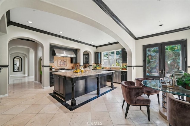 kitchen with french doors, wall chimney exhaust hood, stainless steel dishwasher, light stone counters, and a center island