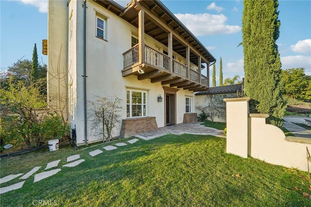 rear view of property with a balcony and a lawn