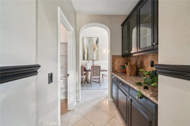 bar featuring light stone counters, decorative backsplash, and dark brown cabinets