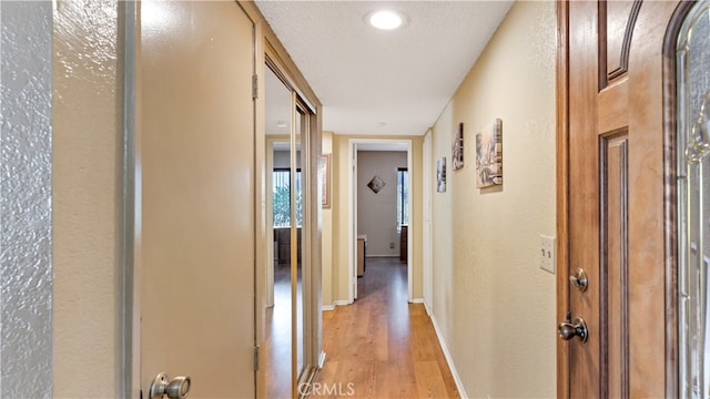 hall featuring light wood-type flooring and a textured ceiling