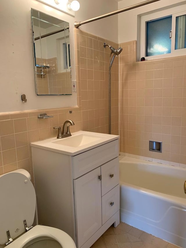 full bathroom featuring tile walls, tiled shower / bath, vanity, and toilet