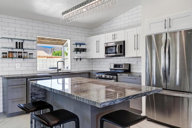 kitchen featuring white cabinets, a kitchen bar, stainless steel appliances, and dark stone counters