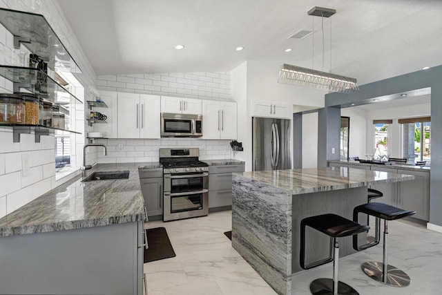 kitchen with sink, stainless steel appliances, decorative light fixtures, lofted ceiling, and a kitchen island