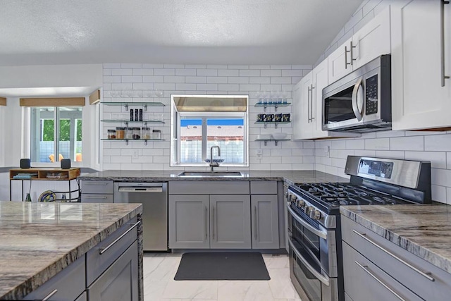 kitchen featuring appliances with stainless steel finishes, backsplash, dark stone counters, sink, and gray cabinets