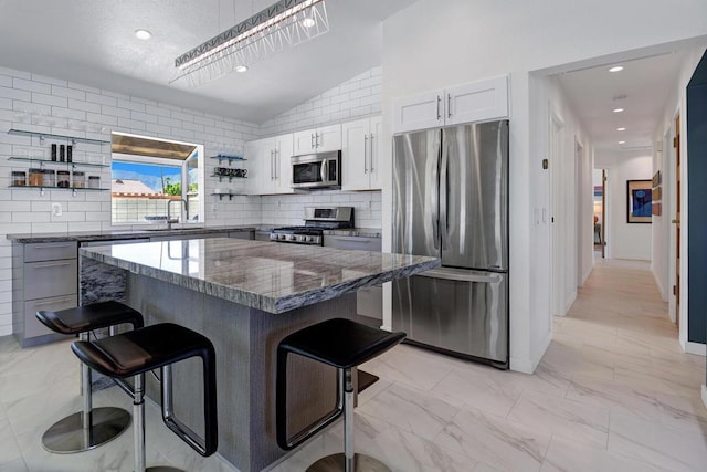 kitchen with a kitchen bar, appliances with stainless steel finishes, white cabinetry, and lofted ceiling