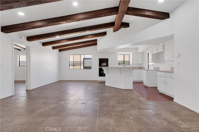 kitchen with a kitchen bar, lofted ceiling with beams, a center island, and white cabinets