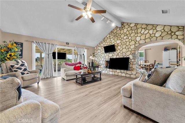 living room featuring lofted ceiling with beams, light wood-type flooring, ceiling fan, and a stone fireplace