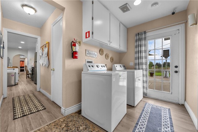 laundry area with cabinets, light wood-type flooring, and washer and clothes dryer