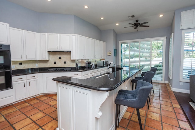 kitchen featuring sink, a center island with sink, white cabinetry, black appliances, and a kitchen breakfast bar