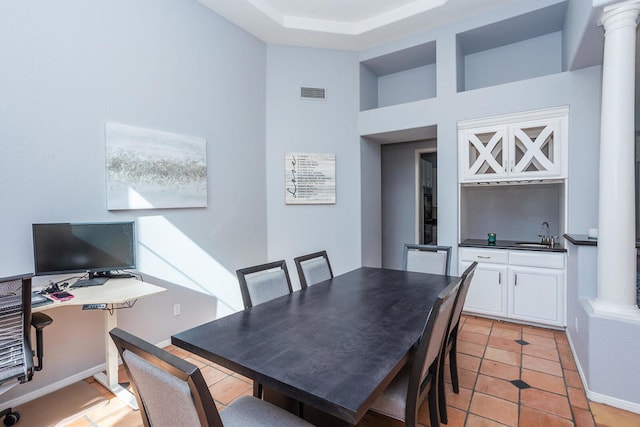 dining room with a towering ceiling, sink, light tile patterned floors, and ornate columns