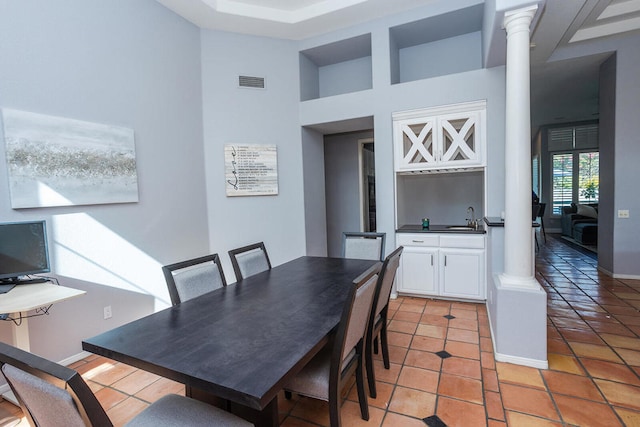 tiled dining room featuring sink, ornate columns, and a high ceiling