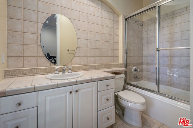 full bathroom featuring tile walls, tile patterned flooring, bath / shower combo with glass door, vanity, and toilet